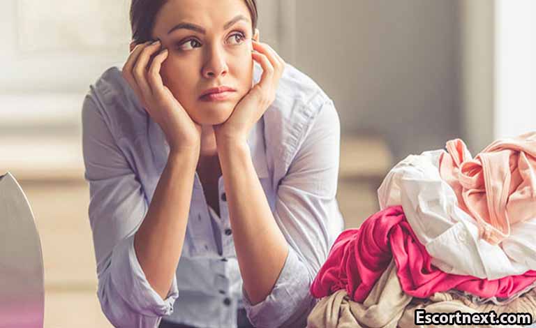 Adult Sex: How Communication Can Improve Your Adult Relationship Woman sitting with her hands cupping her face, looking stressed, beside a pile of laundry and clothes.
